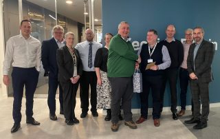 Group of colleagues gathered to celebrate Dougie Hill with a handshake and gift presentation.